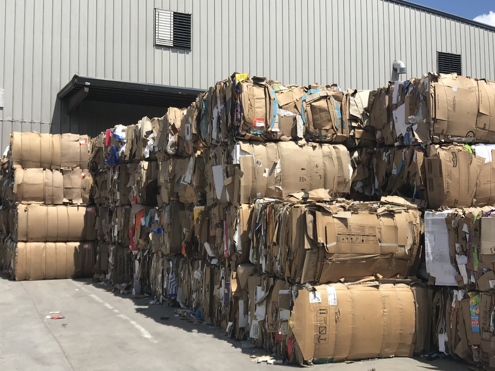 Baled cardboard stacked beside a materials processing building