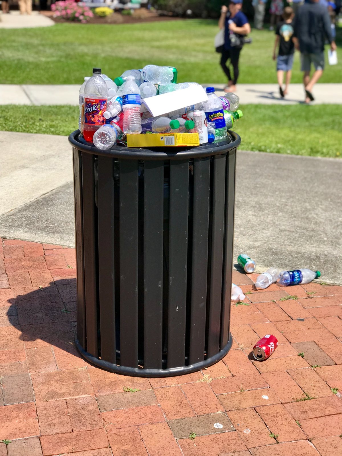 Discarded drink containers and other waste overflowing a public trash bin